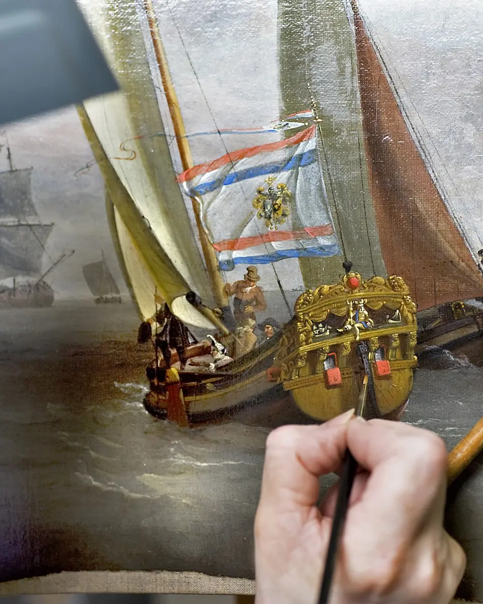 A conservator retouching an old ship painting with a fine brush