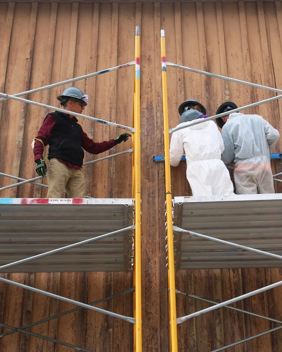 Workers on scaffolding restoring a wooden barn wall