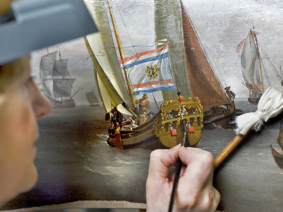 A conservator retouching an old ship painting with a fine brush