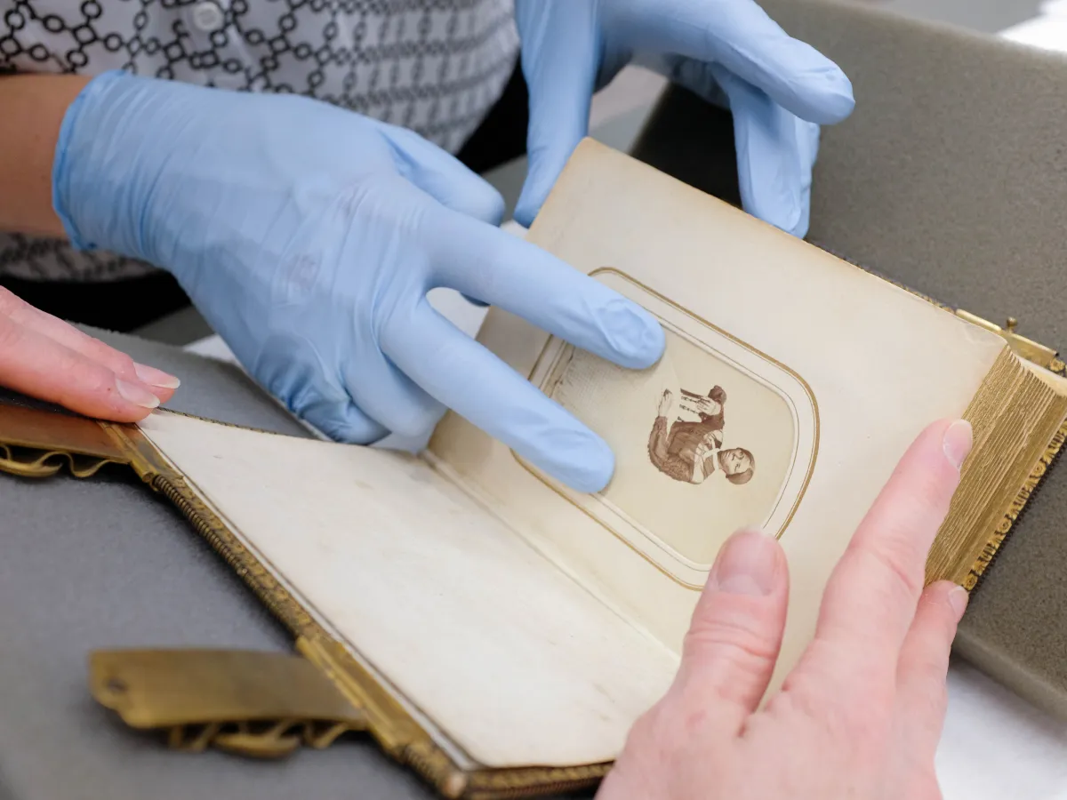 Gloved hands turning the page of a 19th-century photo album
