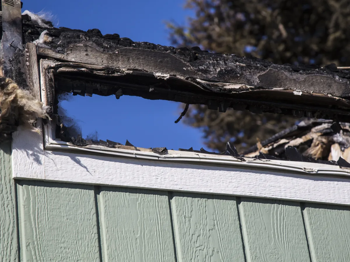 A charred, soot-covered window frame above house siding